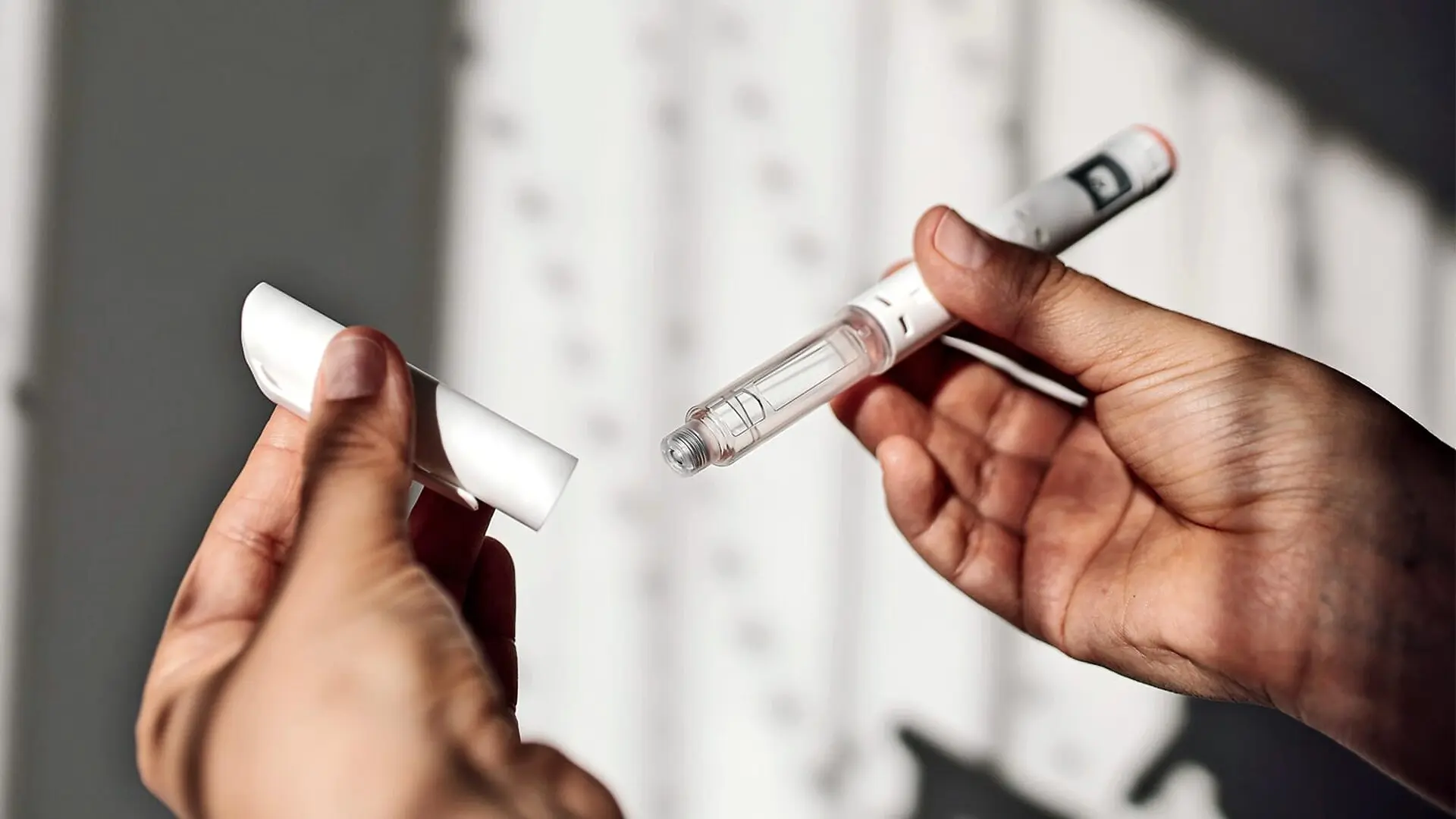 A person holds a GLP-1 medication syringe and its cap.