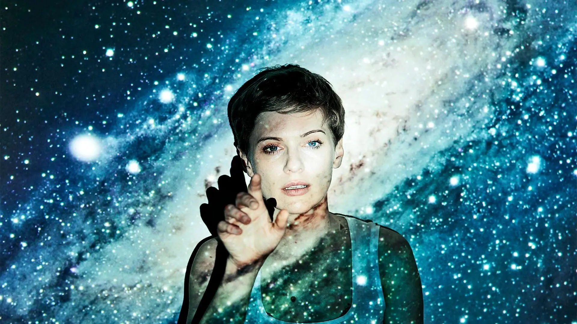A young woman has an image of a galaxy and stars projected over her face.