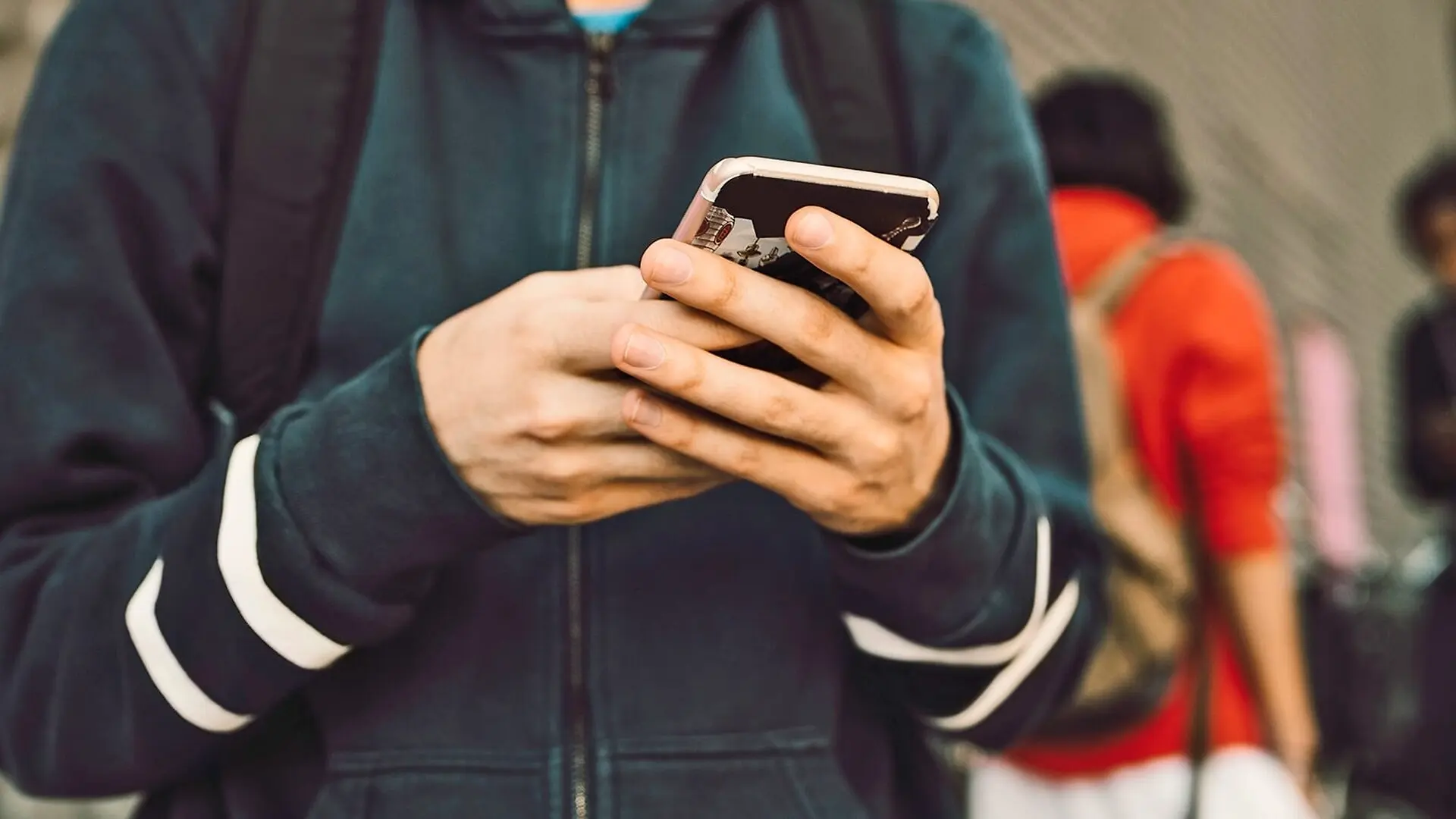 A college student holds a phone in both hands.