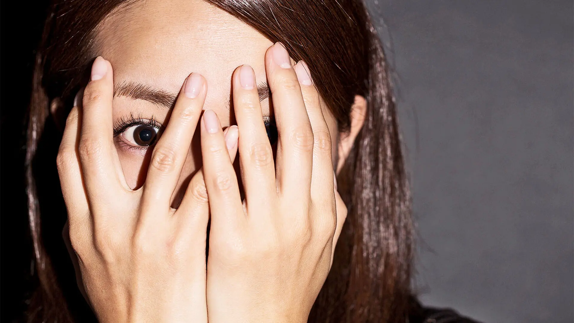 A woman puts her hands over her face and peeks out with one eye.