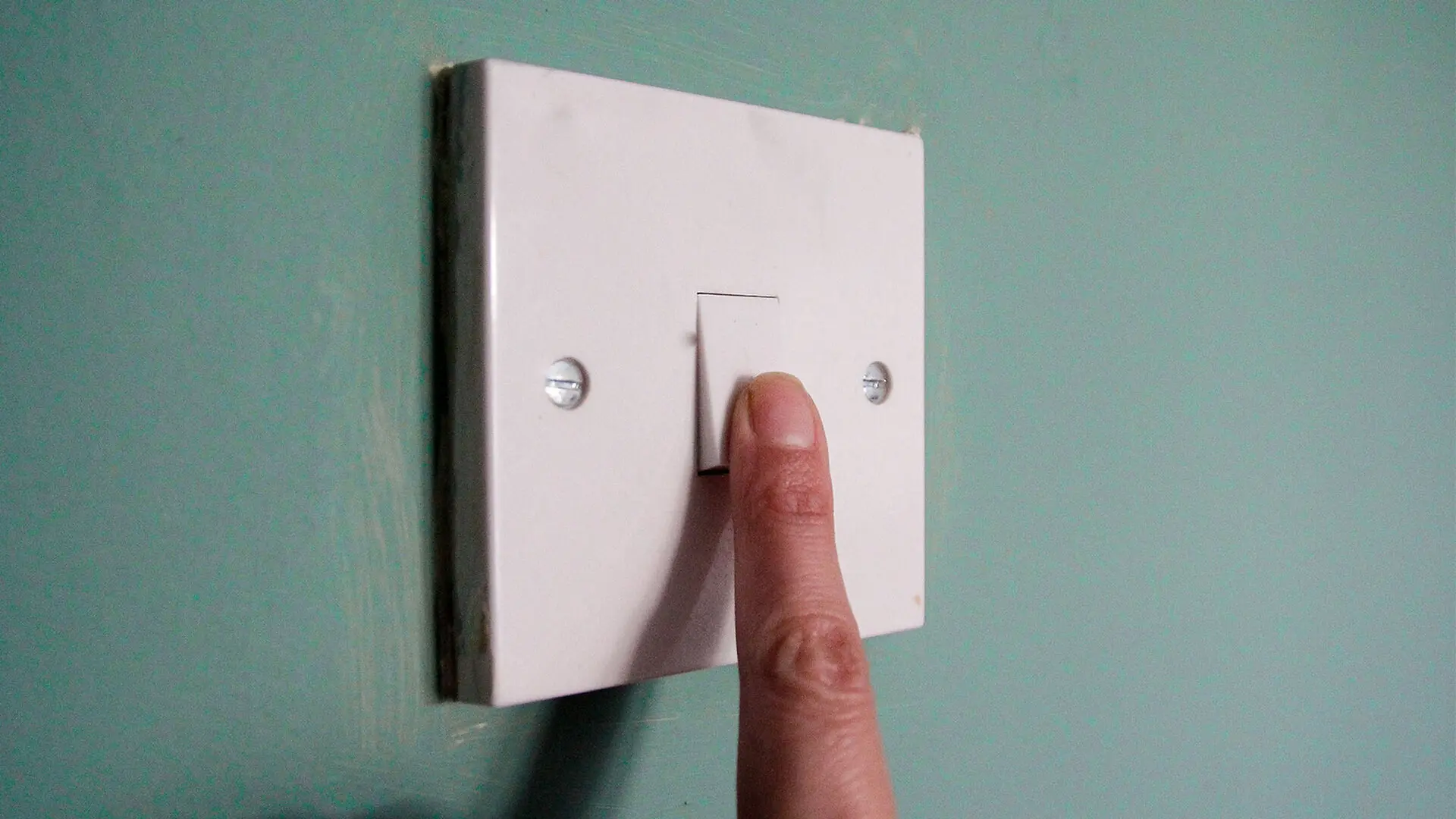 A person touches a switch on a green wall.