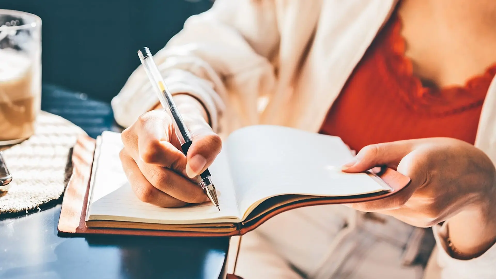 A woman writes in a journal while sitting in a coffee shop.