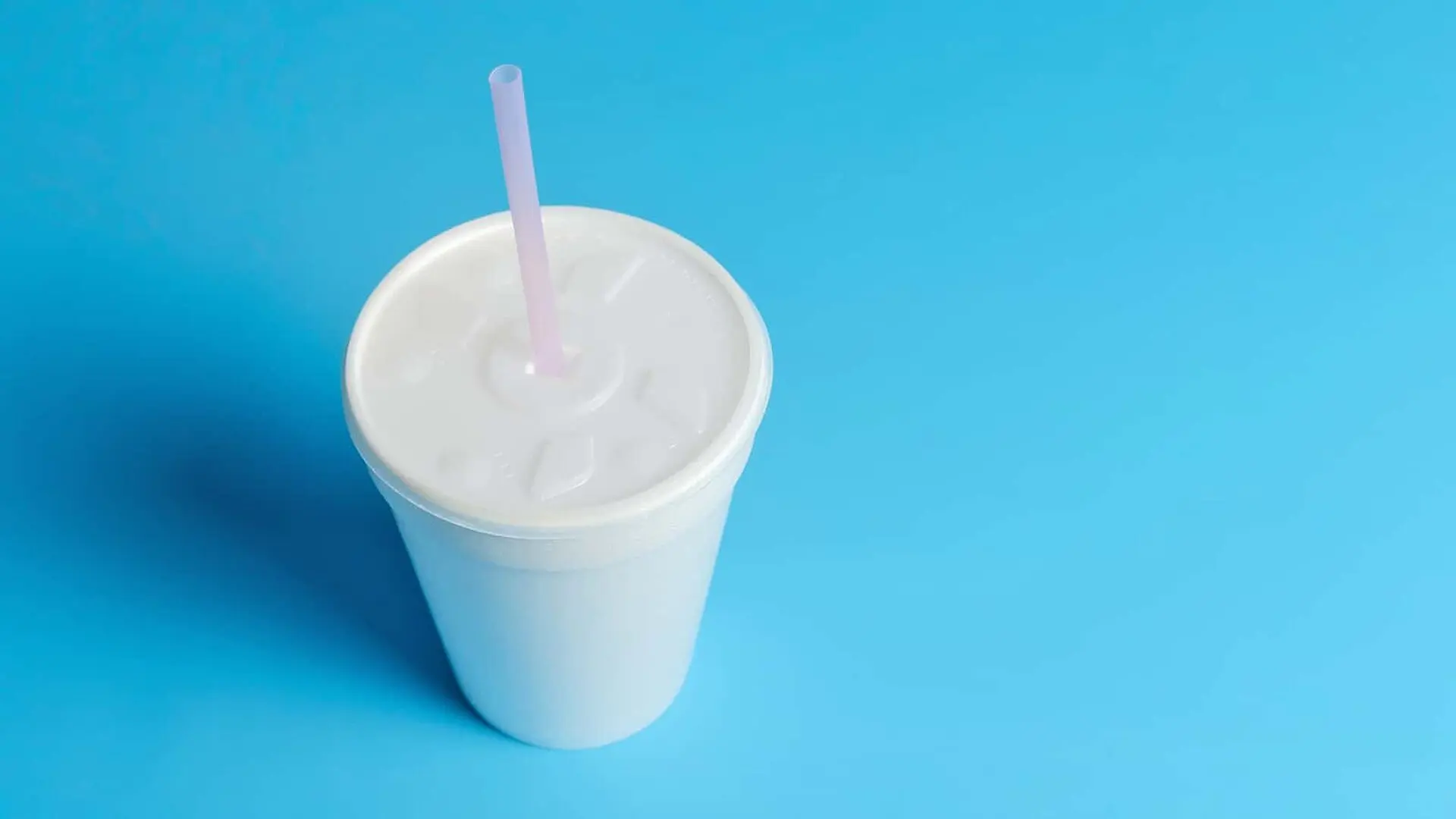 A cup with a plastic lid and straw sits on a blue background.