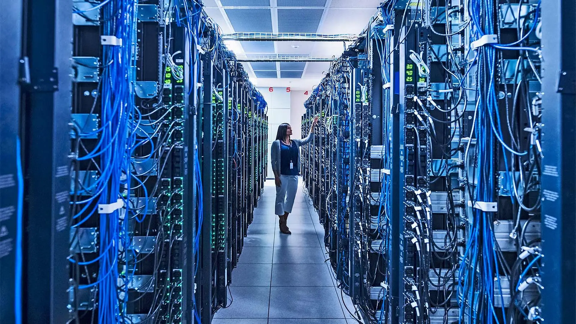 A woman stands between rows of servers in a data center.