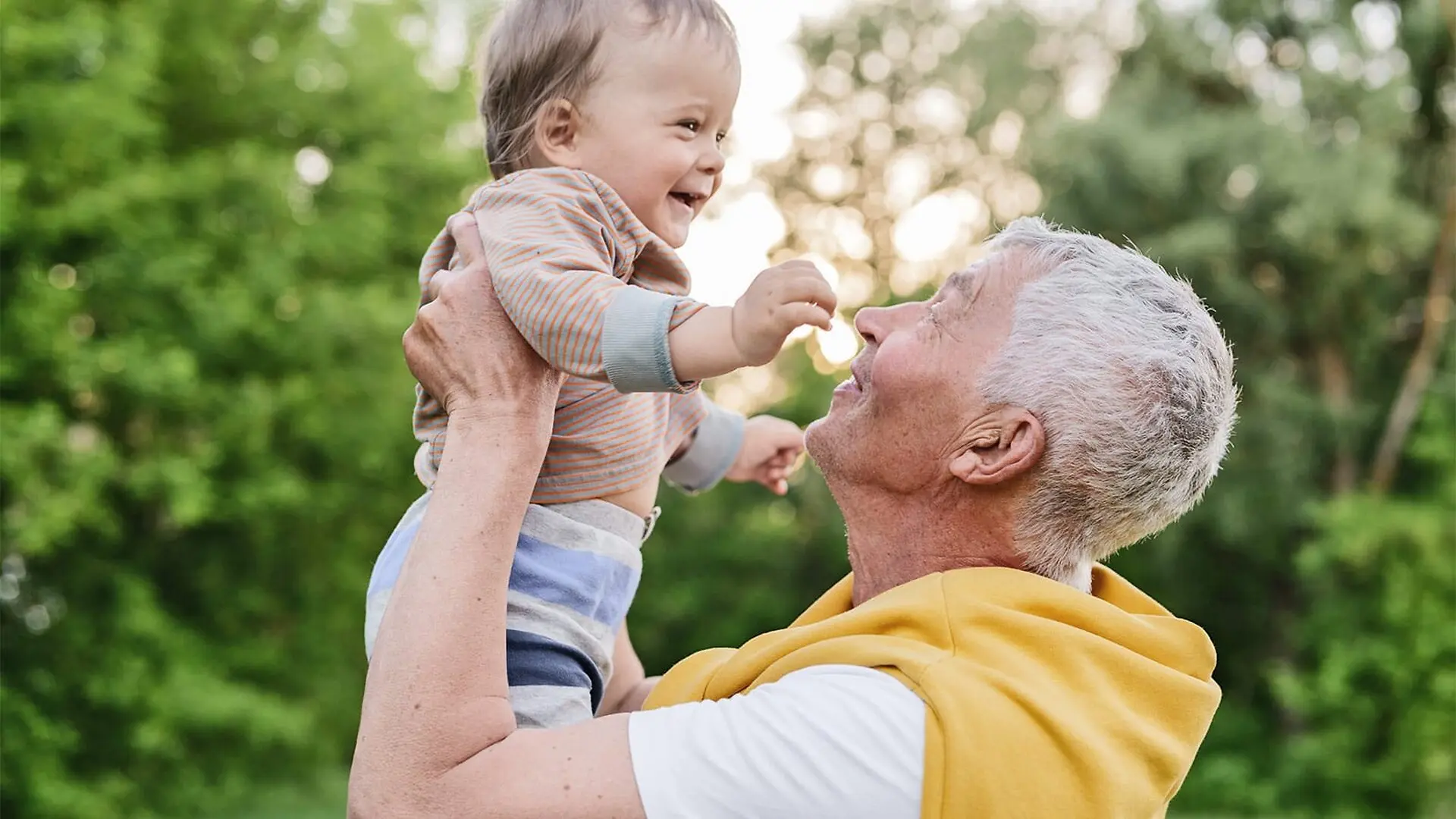 A grandfather picks up his grandchild and lifts her up into the air.