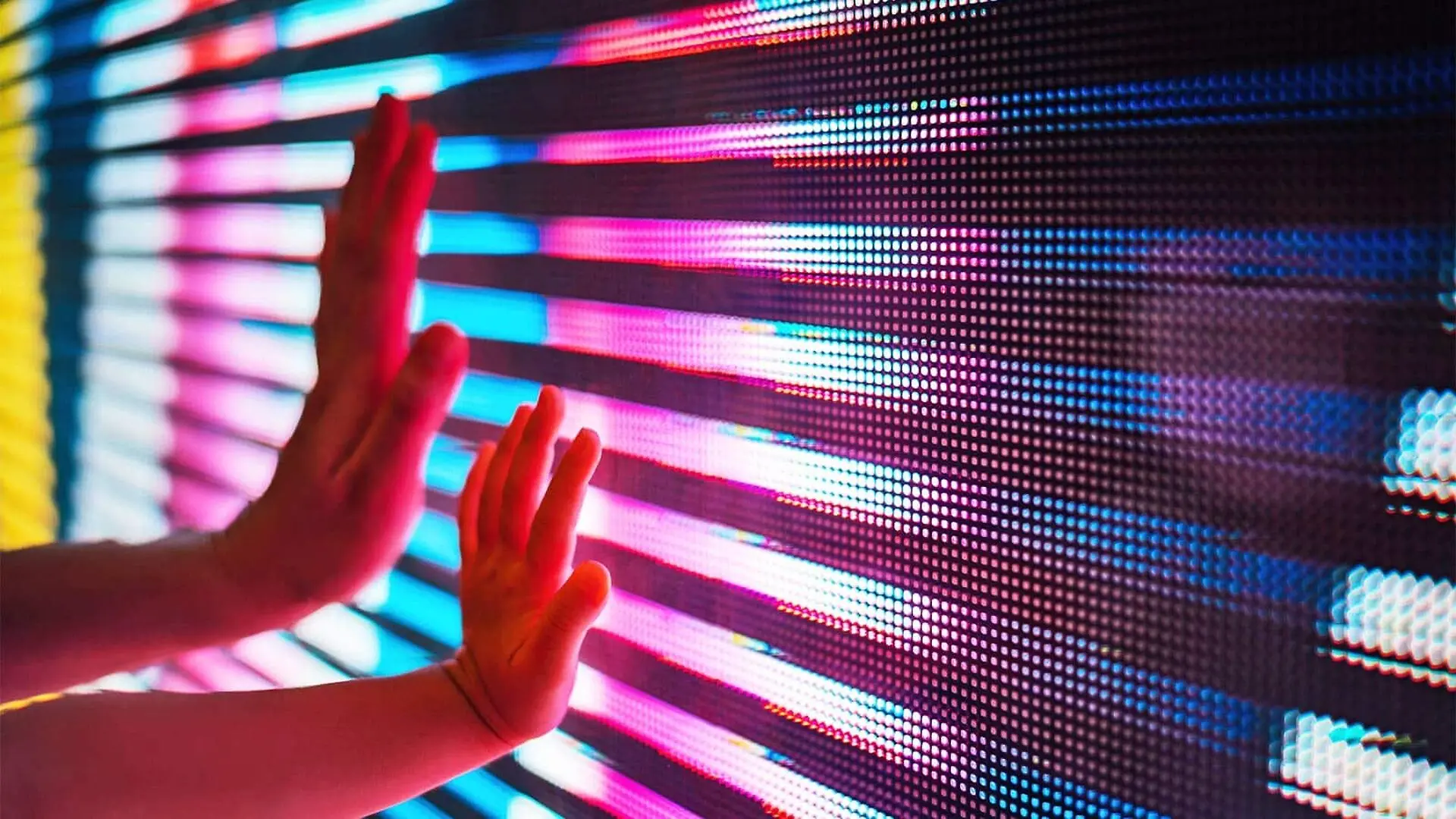 A parent and child place one hand each on a colorful screen made with LEDs.