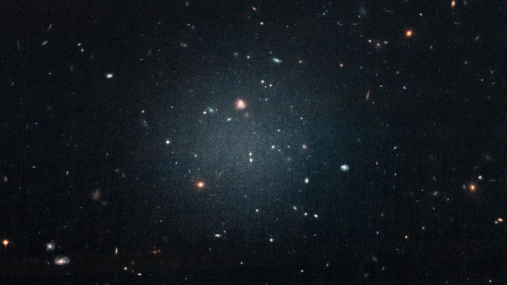 A ghostly, diffuse galaxy floating against a backdrop of distant cosmic structures.