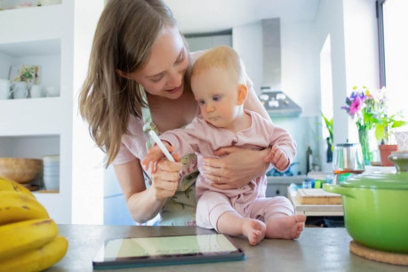 Mom and baby daughter cooking together at home, watching recipes on tablet. Child care or cooking at home concept.